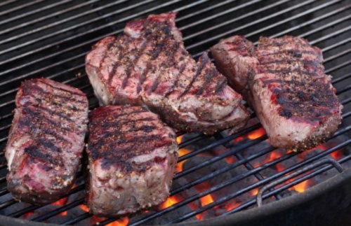 Petite tender beef filet cooking on a hot grill, showing seared grill marks and a juicy, tender interior ready to be served.