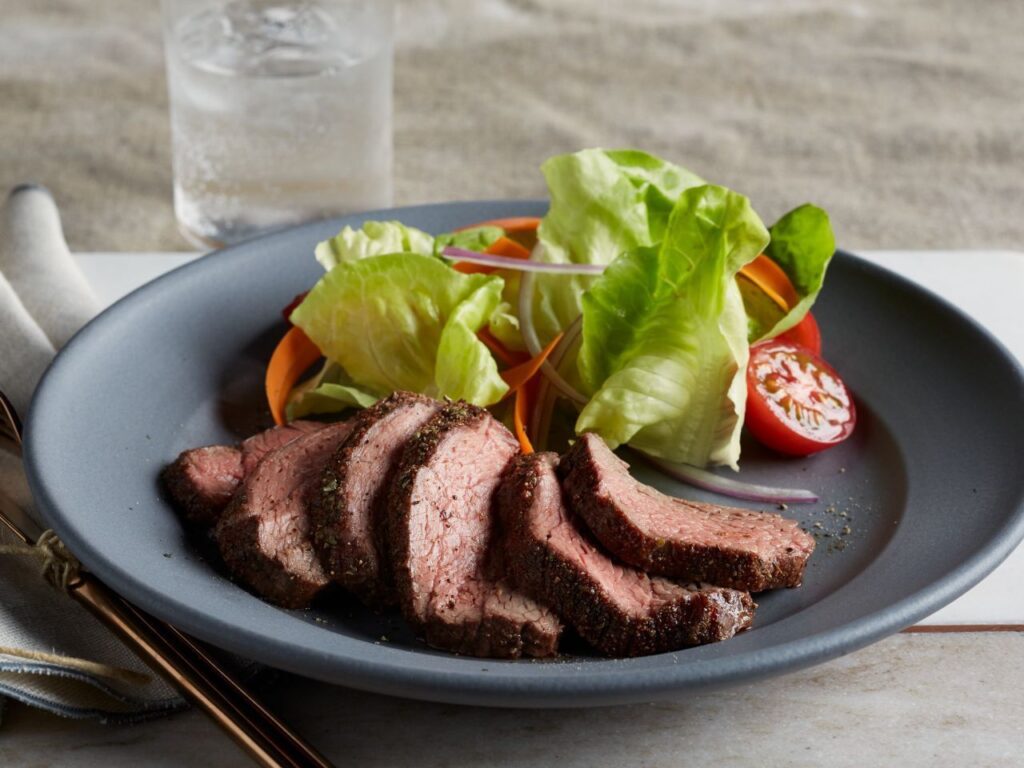Step-by-step preparation of petite tender beef filet, showing seasoning, pan-searing, and resting to achieve a tender, juicy, and flavorful steak.