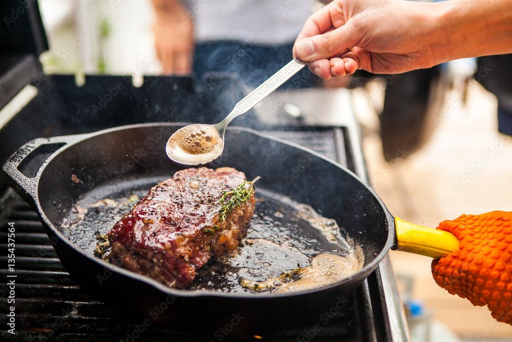 Juicy steak searing in a non stick pan on a stovetop with a golden-brown crust and steam rising, showing proper cooking technique.